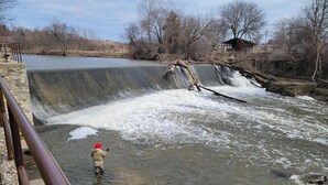 A person fishing by a waterfall in a river.