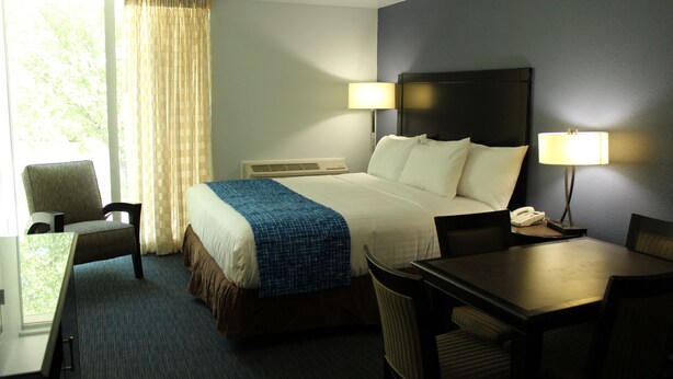 A hotel room with a bed, two bedside lamps, a desk, a chair, and a telephone. - Travelodge by Wyndham Water’s Edge Hotel - Racine (Racine)