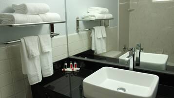 Un bagno moderno con un ampio specchio, due lavabi e porta asciugamani con asciugni piegati.