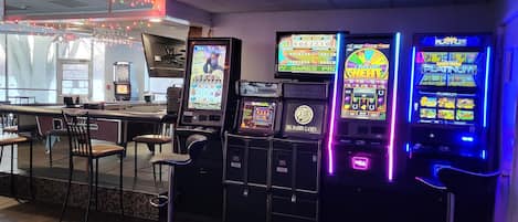 Uma área de bar com máquinas de jogo, banquetas e um alvo de dardos.