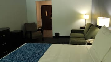 A hotel room with a bed, a chair, a sofa, a lamp, and a desk.