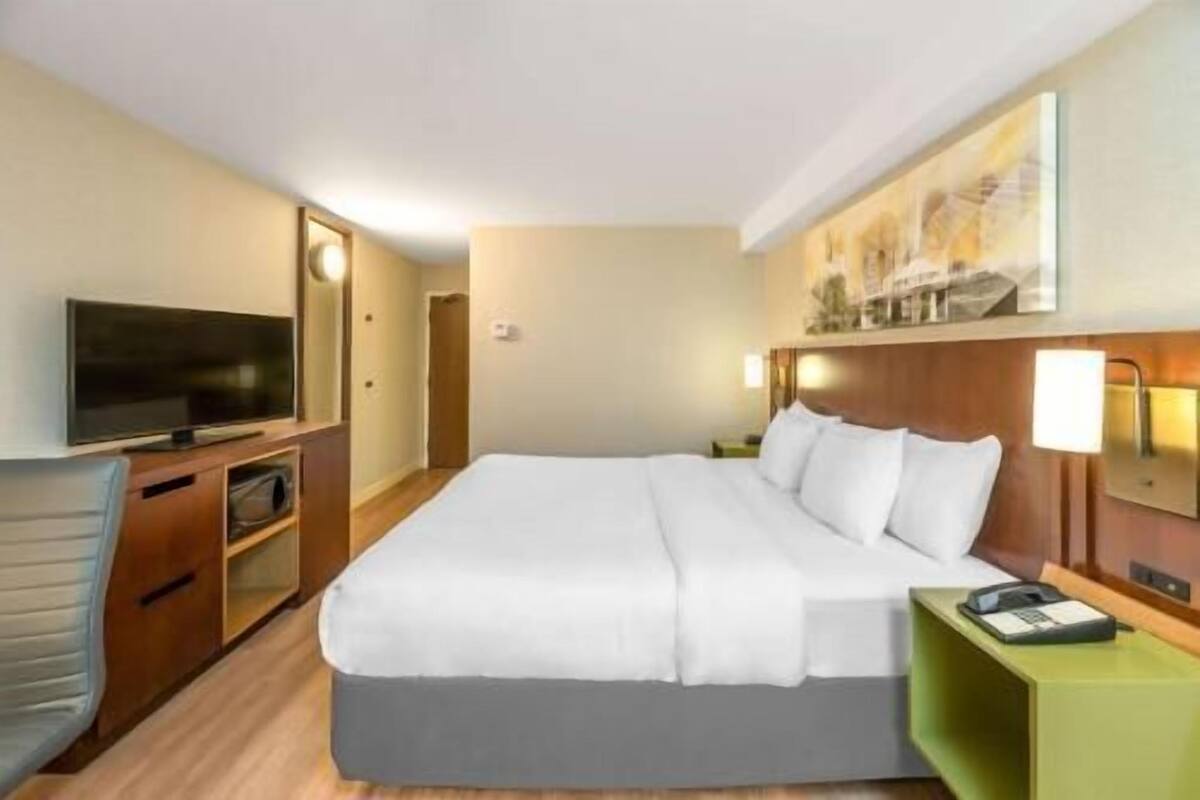 A hotel room with a bed, a television, a desk with a lamp, and a painting on the wall.