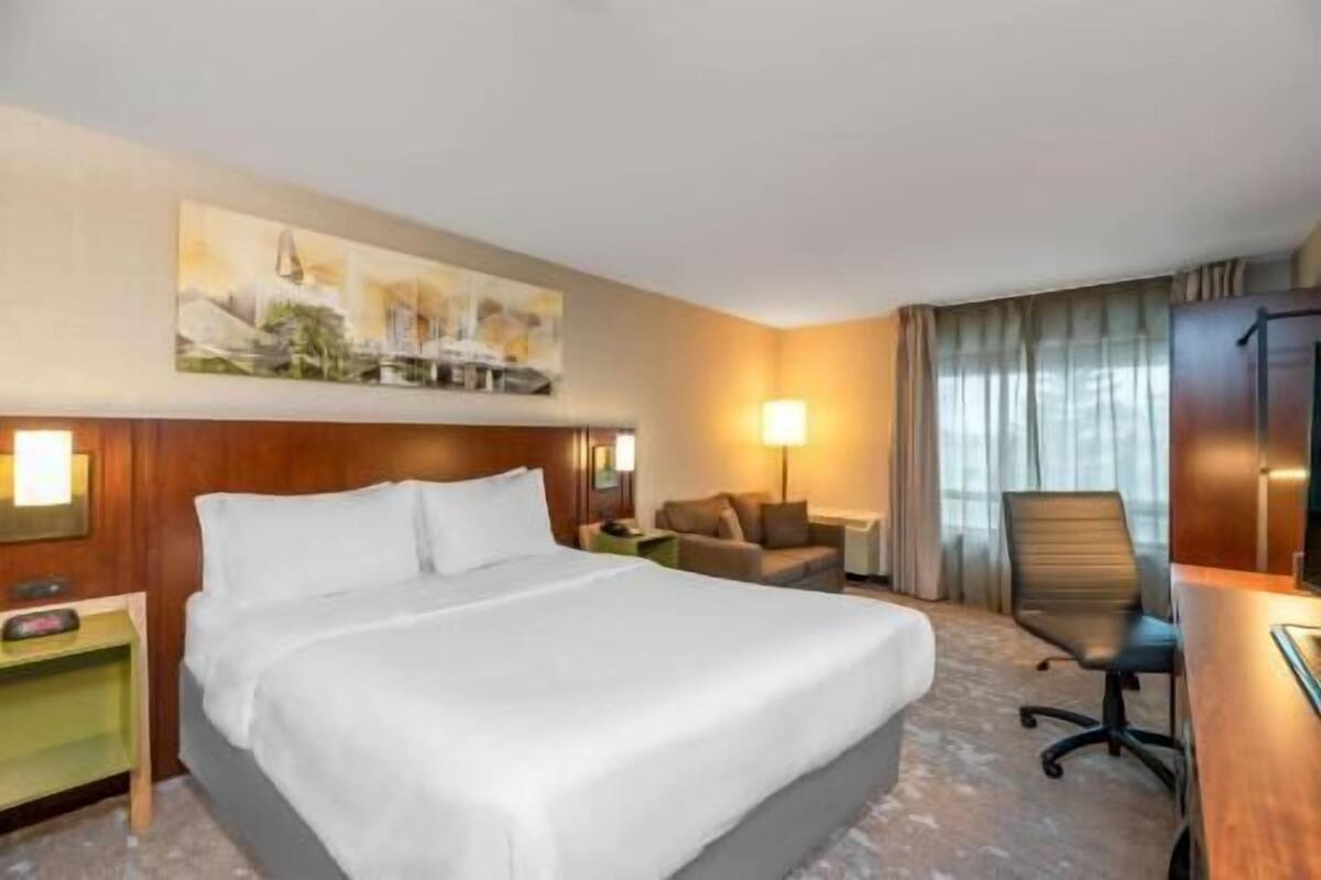 A hotel room with a large bed, a desk, a chair, a lamp, and a painting on the wall.
