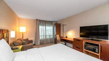 Une chambre d’hôtel comprenant un lit, un bureau, une télévision, un four à micro-ondes et un coin salon avec un fauteuil et un canapé.