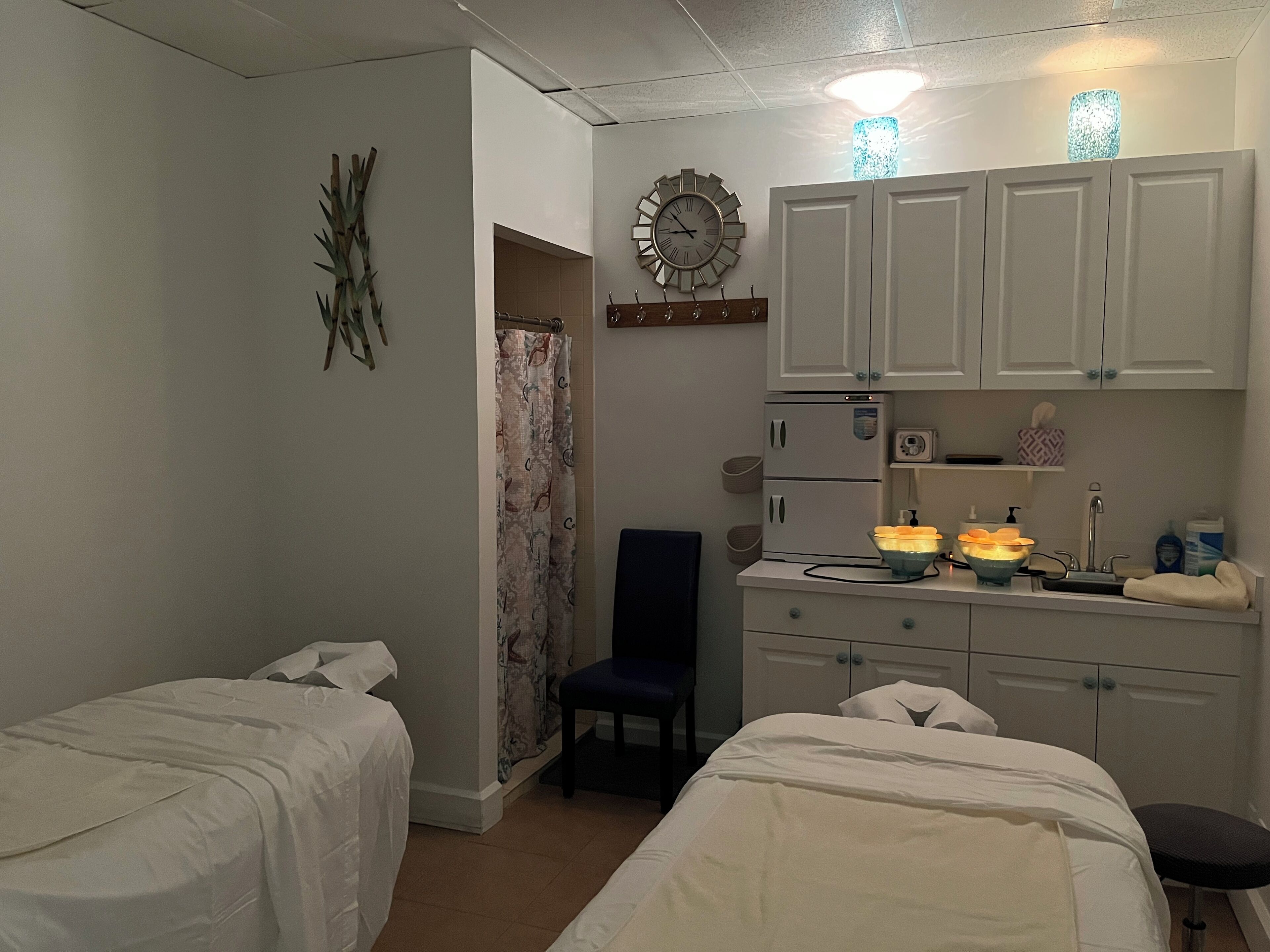A bedroom with two beds, a desk with a chair, a wardrobe, a clock, and a bathroom with a shower curtain.