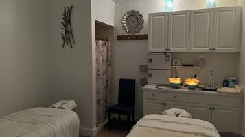 A bedroom with two beds, a desk with a chair, a wardrobe, a clock, and a bathroom with a shower curtain.