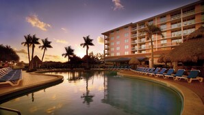Ein Hotelpool mit Liegestühlen, Palmen und einem Gebäude mit Balkonen.