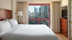 A hotel room with a large bed, a television, a dresser, and a window with a city view.