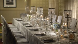 A long banquet table set with crystal candle holders, silverware, and white tablecloths.