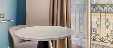 Una habitación con una mesa redonda, una silla, una ventana con cortinas y vistas a edificios.