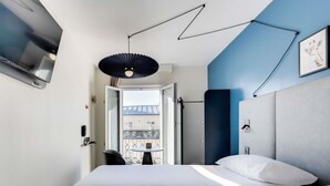 A modern hotel room with a bed, a desk, and a balcony view. - ibis Paris Père Lachaise (Paris)