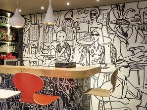 A bar area with a counter, hanging pendant lights, and a wall with black and white illustrations. - ibis Paris Père Lachaise (Paris)