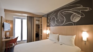 Habitación de hotel con cama, escritorio, silla, televisor y un pared con un dibujo en la pizarra.