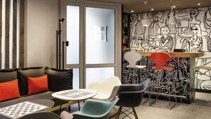 A modern lounge area with a sofa, chairs, a table, and a mural on the wall. - ibis Paris Père Lachaise (Paris)