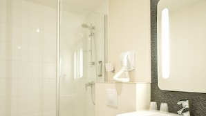 Un baño moderno con ducha envuelta en vidrio, inodoro blanco, lavabo con espejo y toallero.