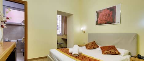 A hotel room with a bed, a desk, and a bathroom visible through an open door.