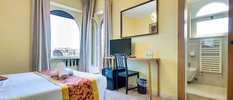 A hotel room with a bed, desk, chair, and a view of the city through large windows.