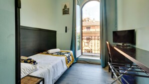 A hotel room with a bed, a desk, a TV, and a window with a view of buildings.