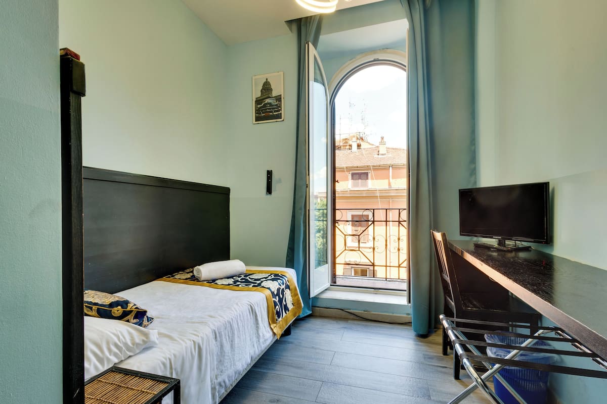 Une chambre d’hôtel avec un lit, un bureau, une télévision et une fenêtre donnant sur des immeubles.