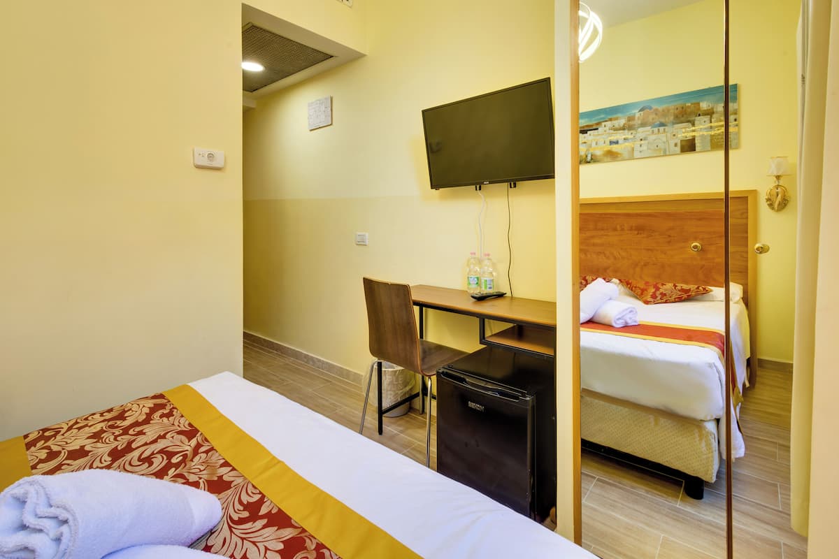 Une chambre d’hôtel comprenant un lit, un bureau, une chaise, un petit réfrigérateur, un téléviseur fixé au mur et un tableau au-dessus du lit.