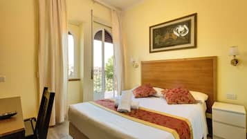 Une chambre d’hôtel avec un grand lit, une tête de lit en bois, un tableau au mur, une table de chevet avec une lampe et une vue sur l’extérieur par une porte ouverte.
