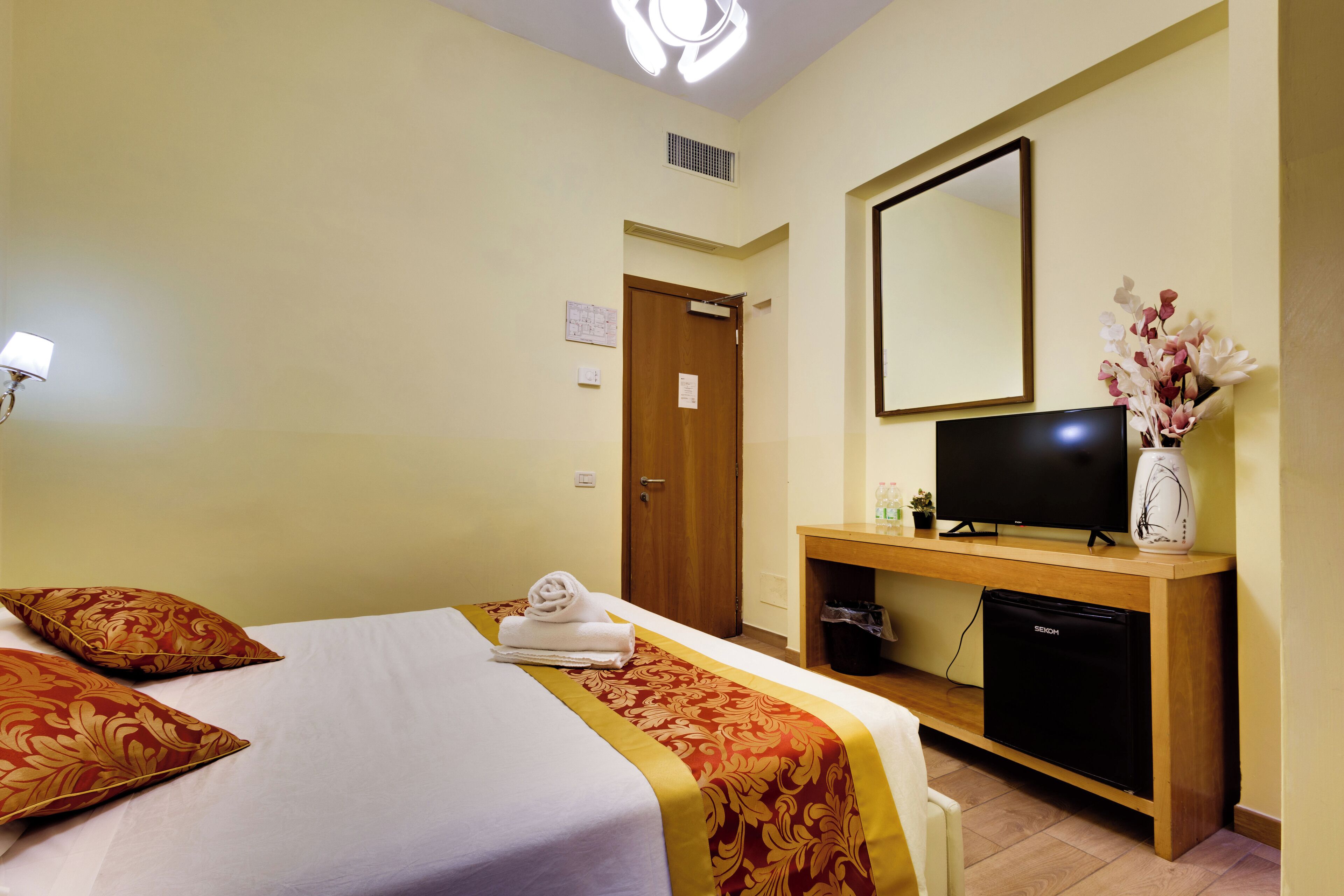 A hotel room with a bed, a TV, a small fridge, and a mirror on the wall.