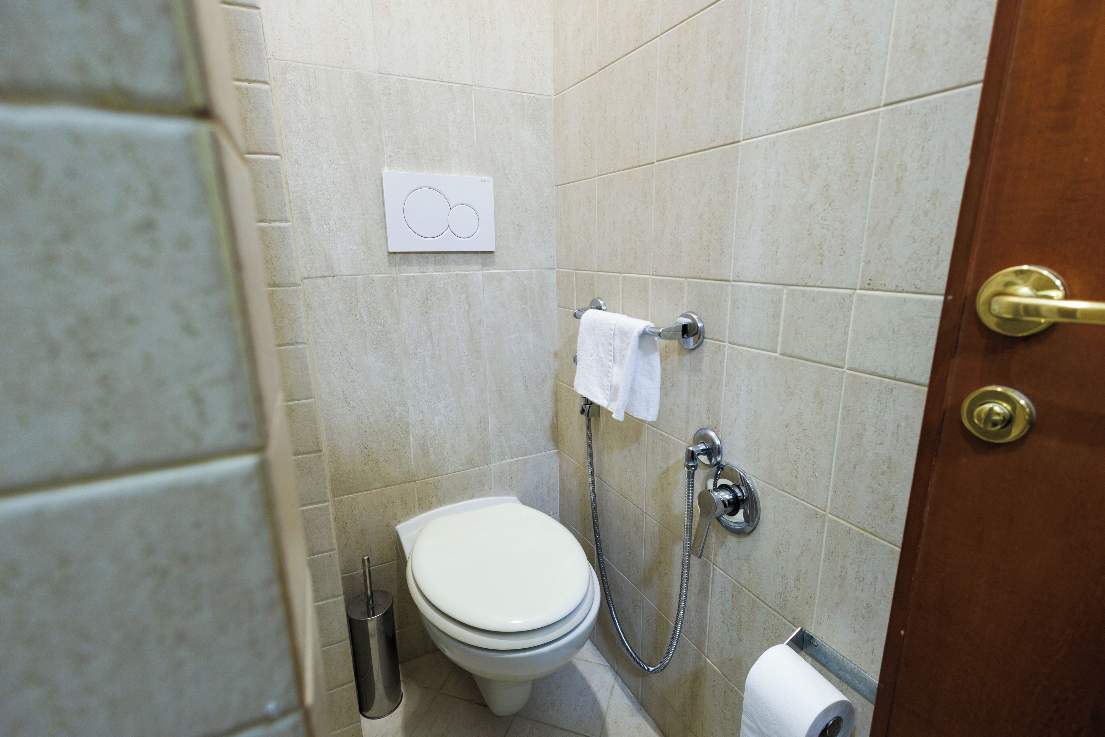 A bathroom with a toilet, a towel rack, a paper towel dispenser, and a toilet paper roll.