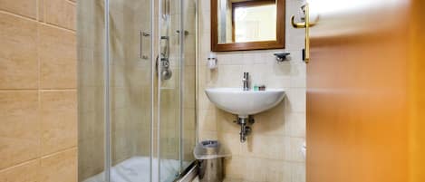 A bathroom with a glass-enclosed shower, a sink, and a trash can.