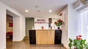 A hotel reception area with a wooden reception desk, a sign reading "HOTEL TERMINAL," and potted plants. - Hotel Terminal (Rome)