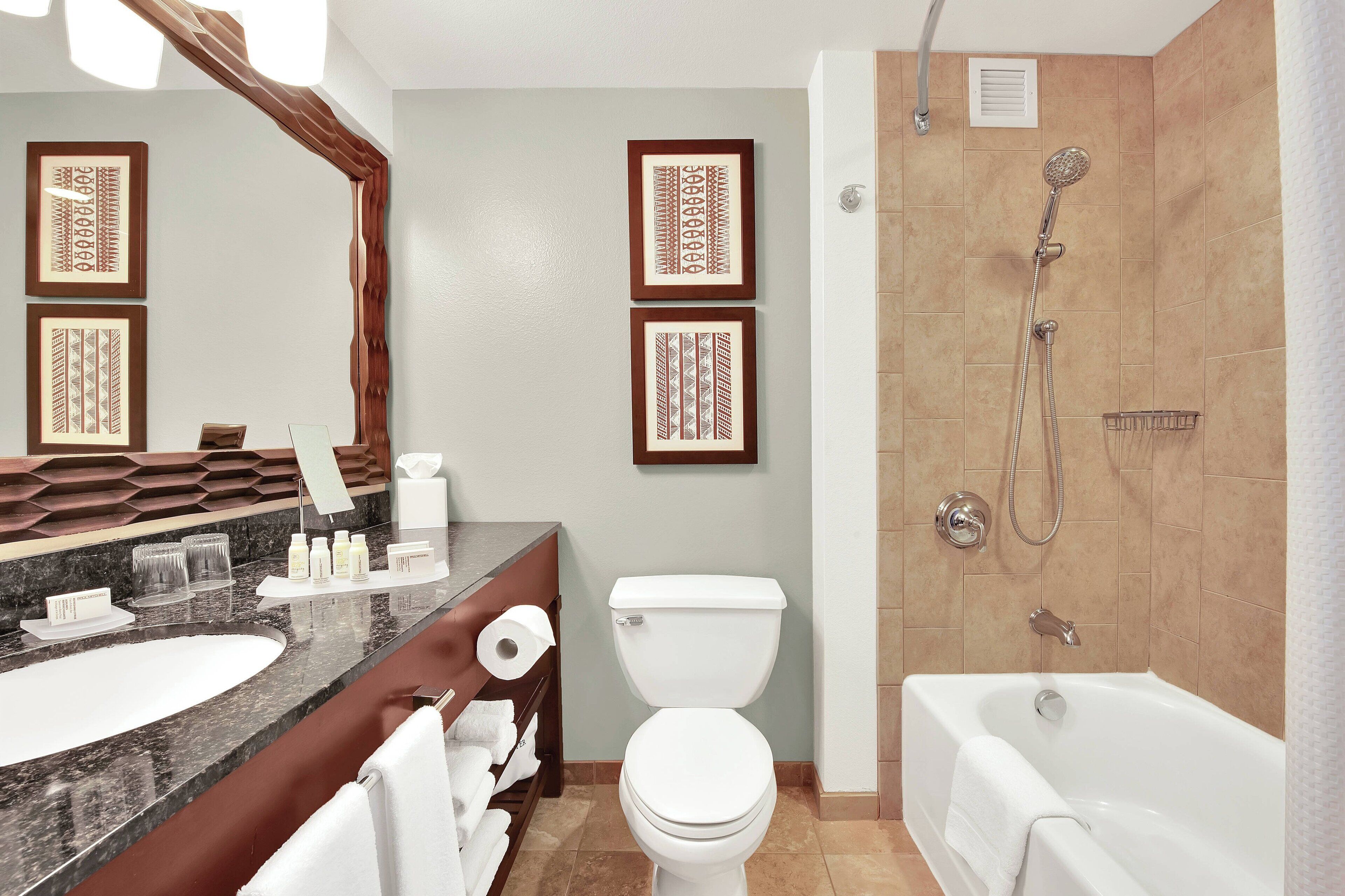 A modern bathroom with a marble sink, a toilet, a bathtub, and framed wall art.