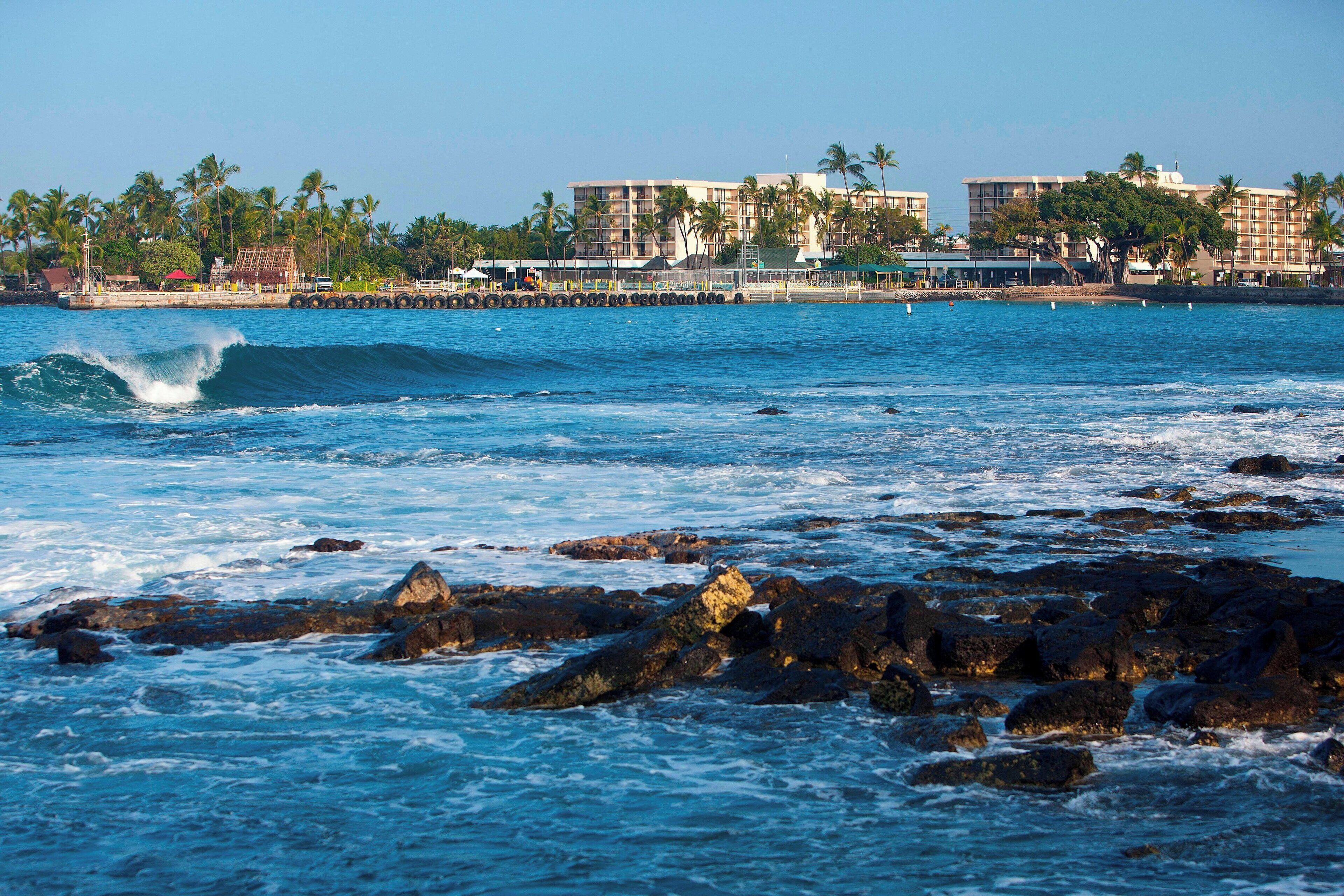 A coastal hotel with multiple buildings, a pier, and palm trees.