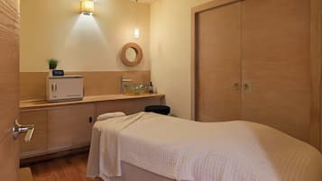 A hotel room with a bed, a bedside table with a lamp, a small plant, a round mirror, and a wardrobe.