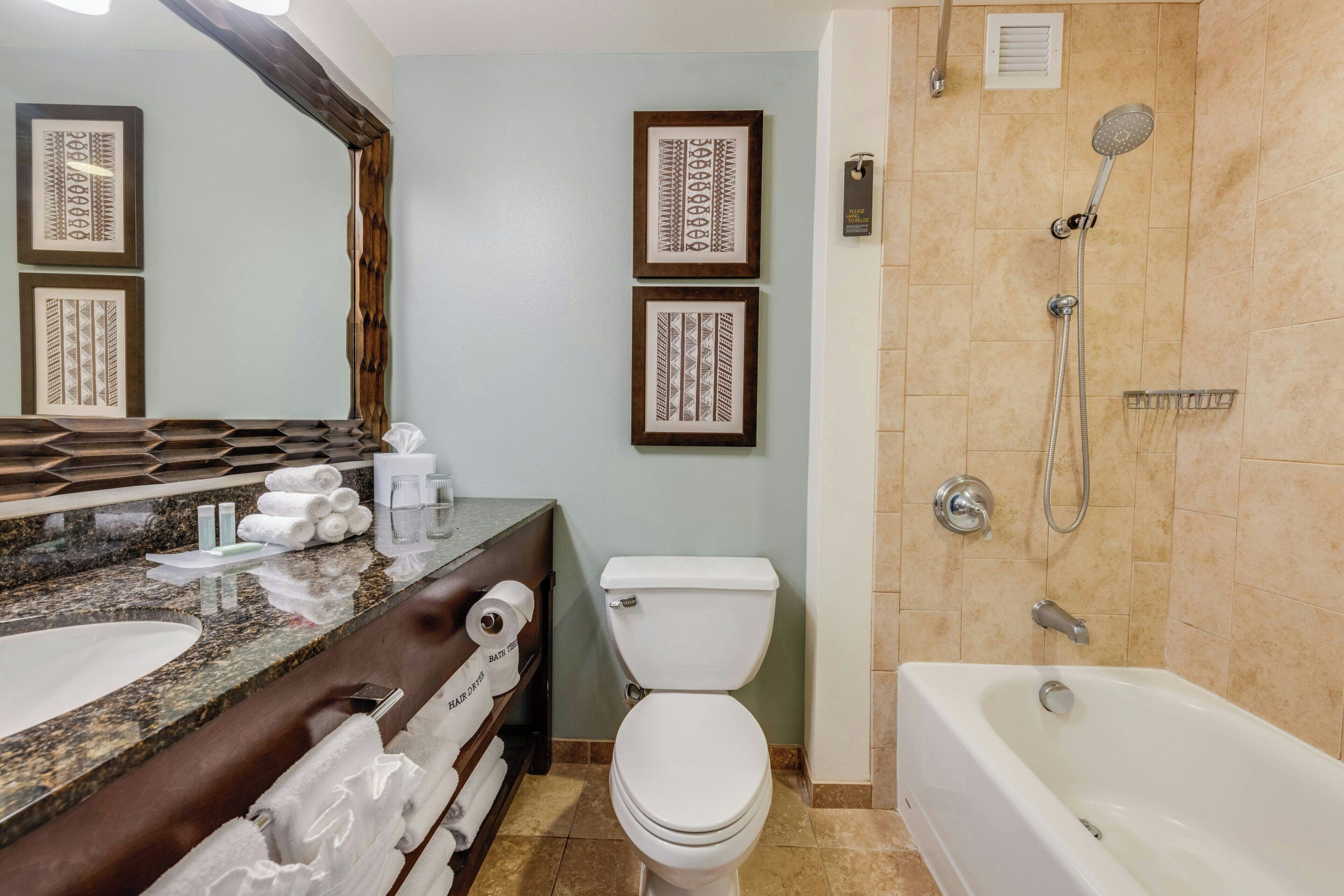 Un baño con lavamanos de mármol, inodoro, bañera y cuadros decorativos en la pared.