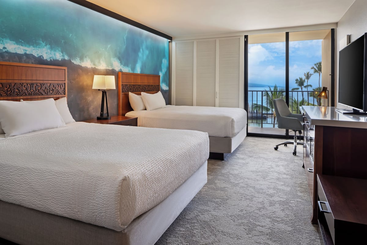Une chambre d’hôtel avec deux lits, un bureau, une chaise, une télévision et un balcon avec vue sur l’océan.