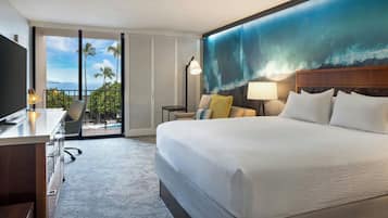 A hotel room with a large bed, a desk, a chair, a desk lamp, and a view of the ocean through a sliding door.