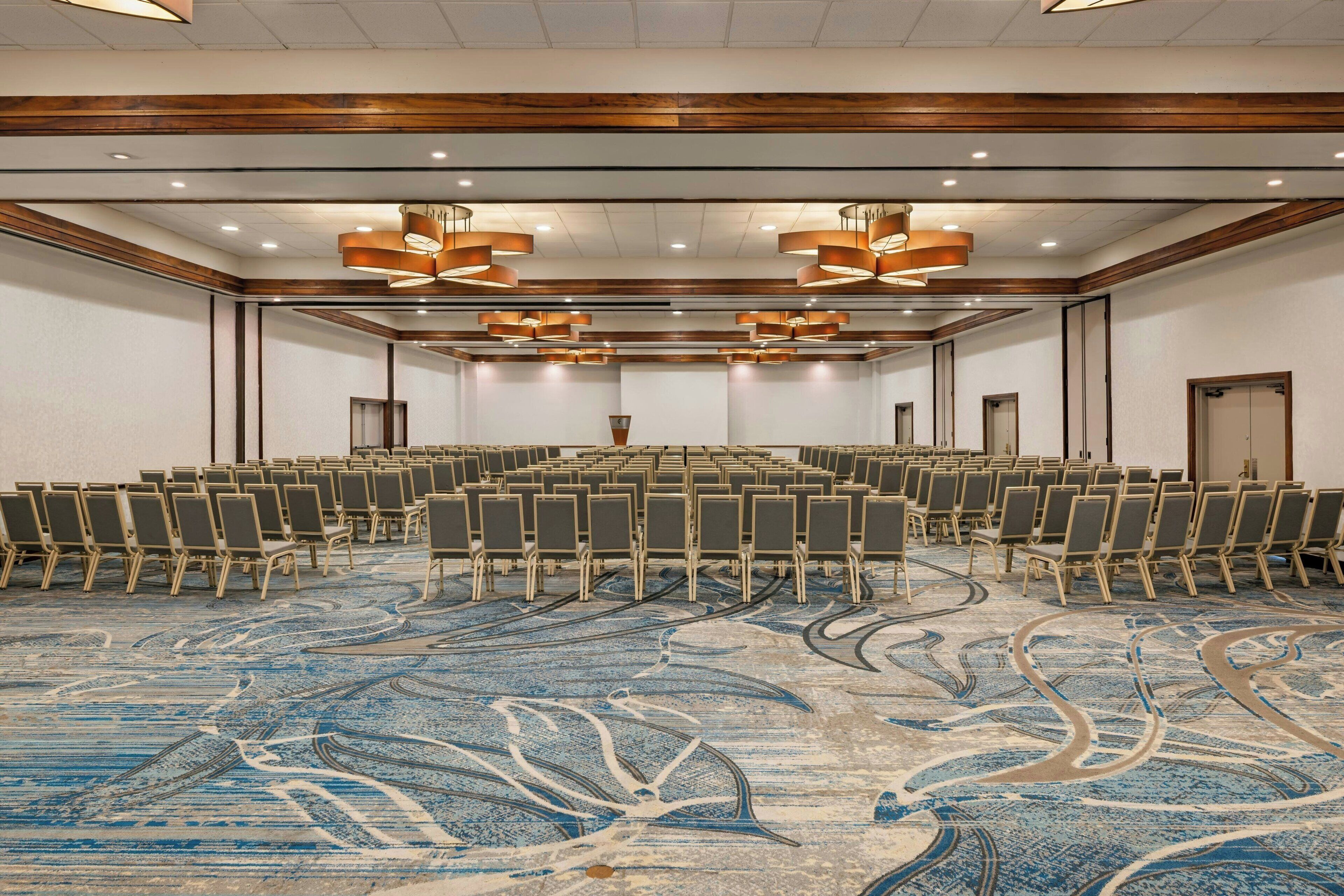 Une salle de conférence avec des rangées de chaises, une moquette à motifs et des luminaires modernes.