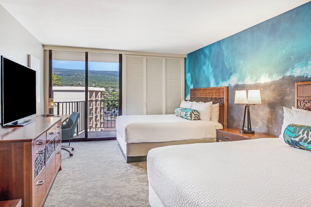 Une chambre d’hôtel avec deux lits, un bureau, une télévision et un balcon donnant sur la ville.