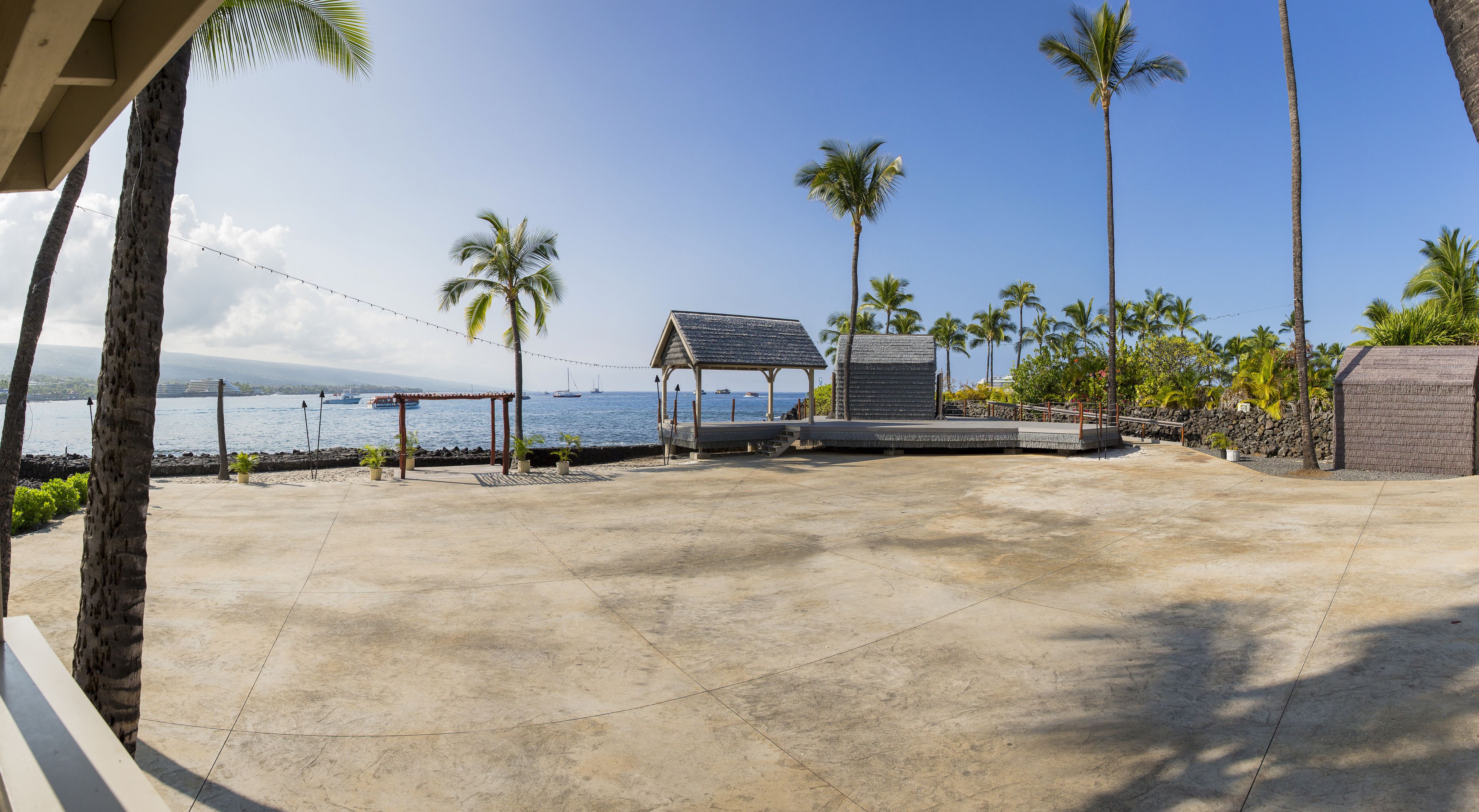 A beachside area with a concrete patio, a gazebo, and palm trees.