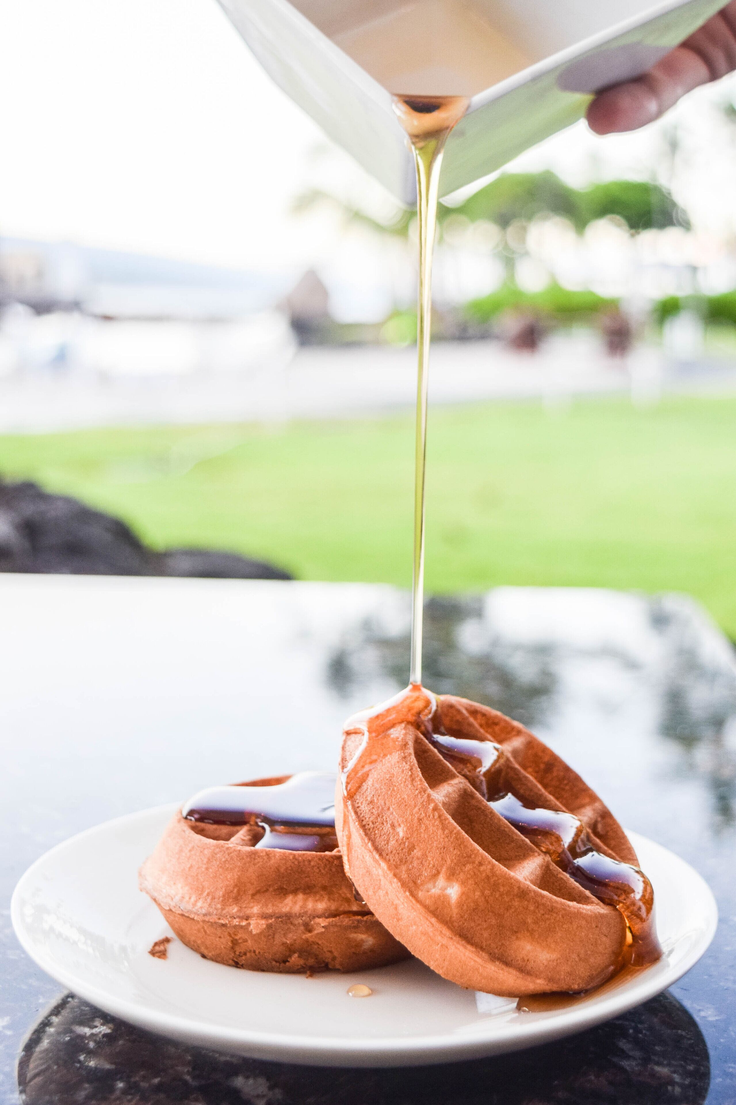 A waffle with syrup being poured over it.