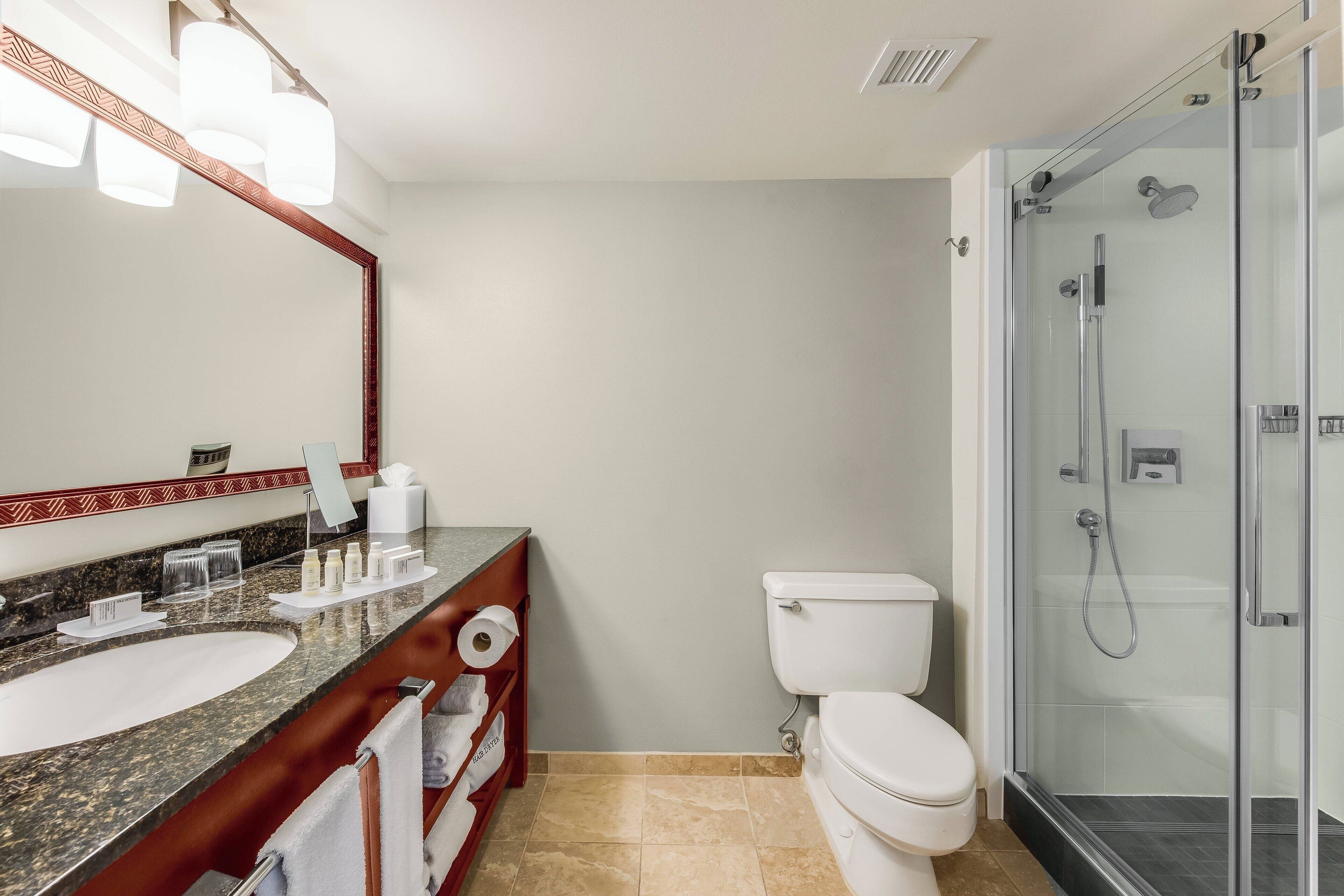 Un baño moderno con lavamanos de granito, inodoro y cabina de ducha con paredes de vidrio.