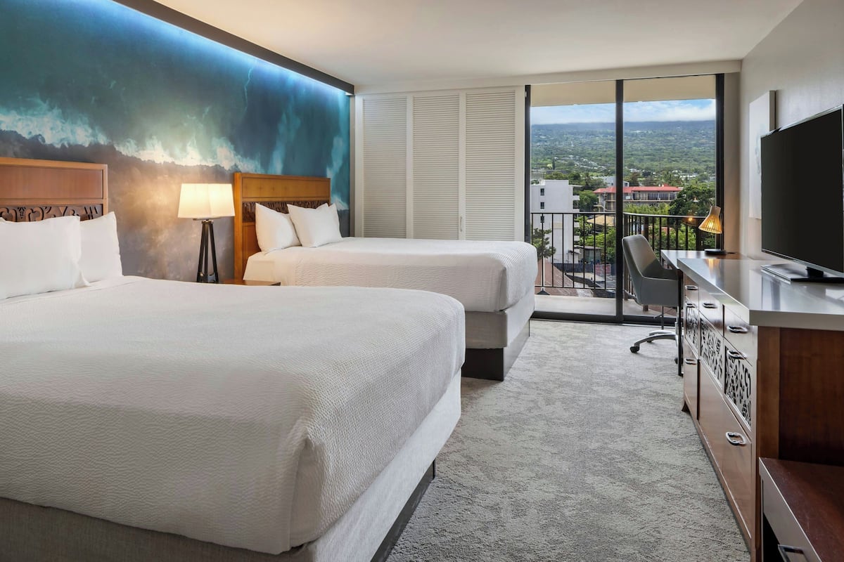 Une chambre d’hôtel avec deux lits, un bureau, une télévision et un balcon donnant sur la ville.