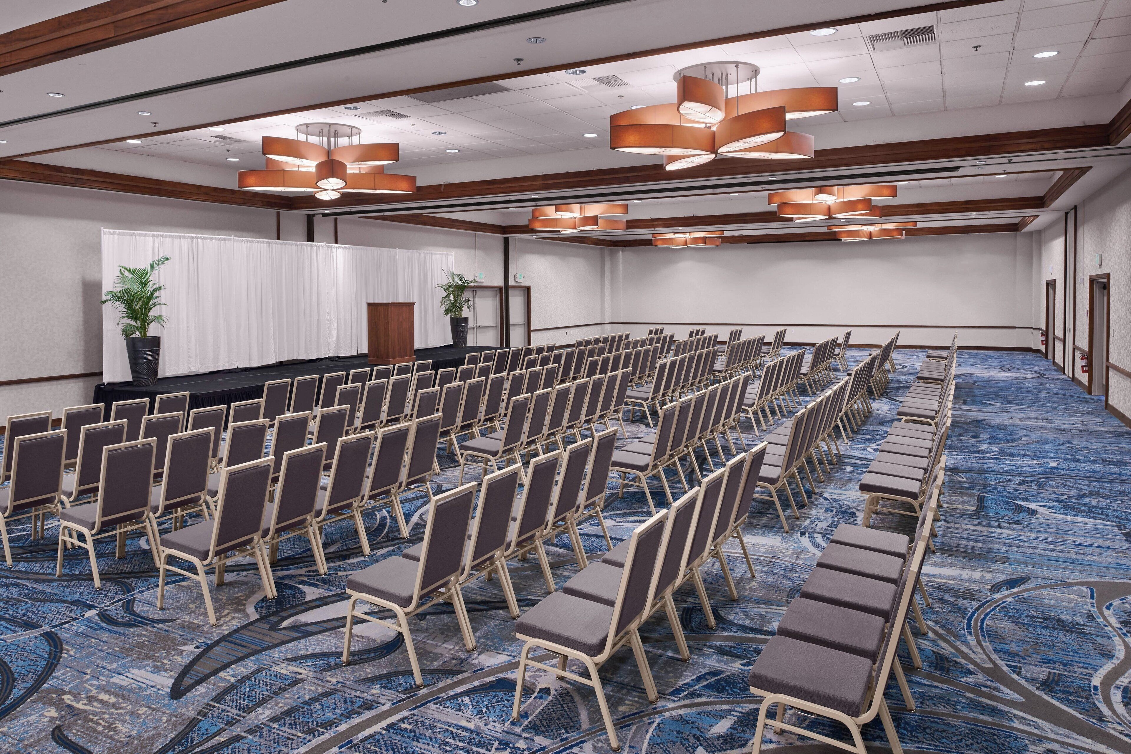 Un salón de conferencias con filas de sillas, un escenario y una alfombra azul.