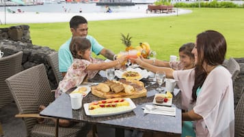 Une famille est assise à une table en plein air, profitant de la vue sur la plage et l’océan.