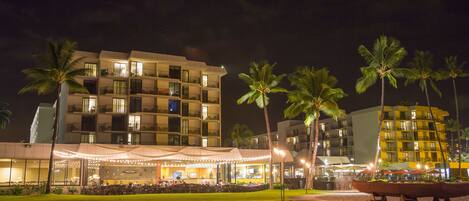 A hotel with multiple balconies, a covered outdoor seating area, and palm trees.