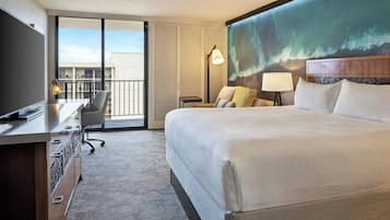Habitación de hotel con una cama grande, un escritorio con silla, una computadora portátil y vistas al exterior a través de una puerta corredera.