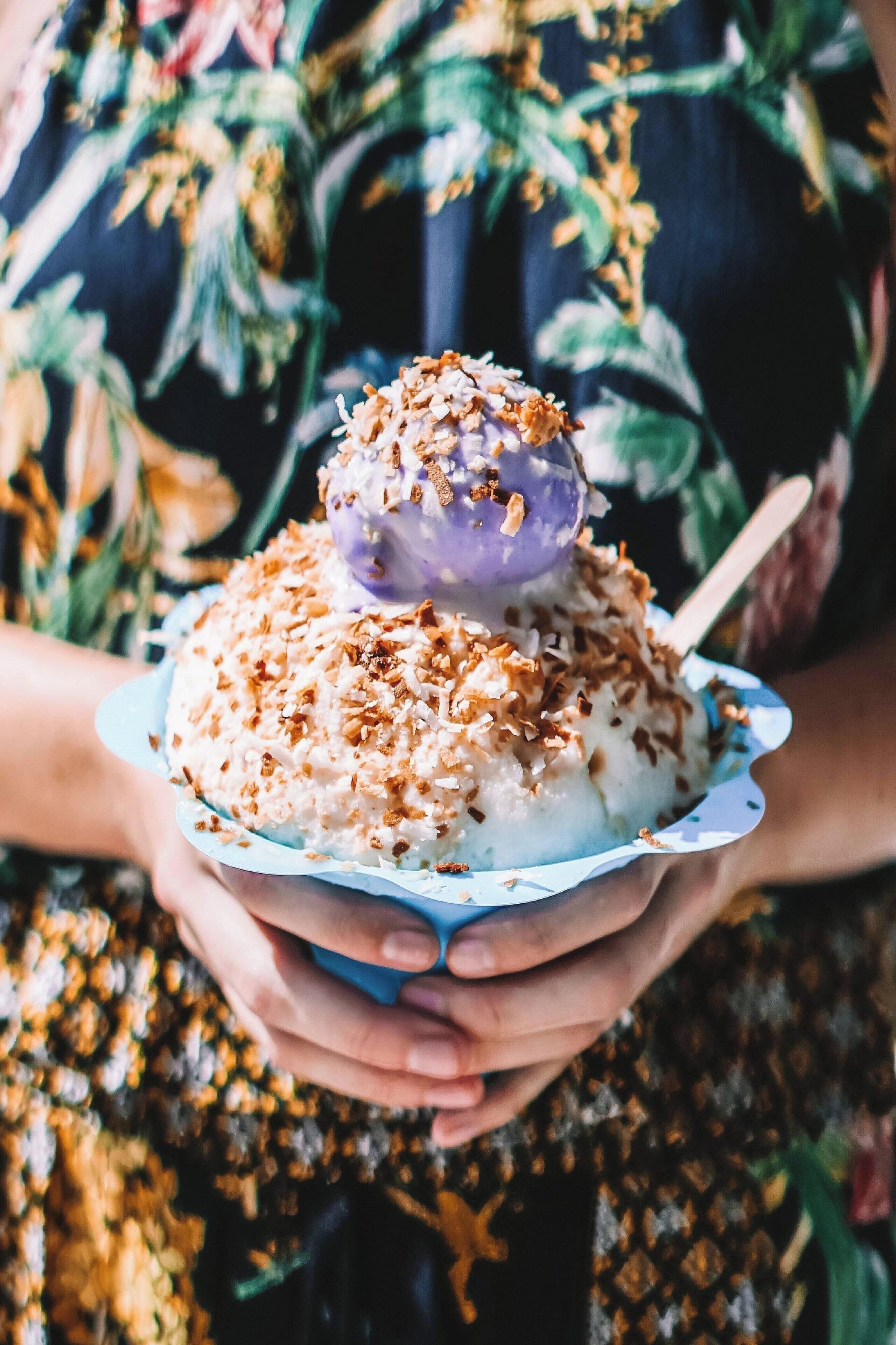 Una persona sosteniendo un bol de postre cubierto con hojuelas de coco y un topping morado.