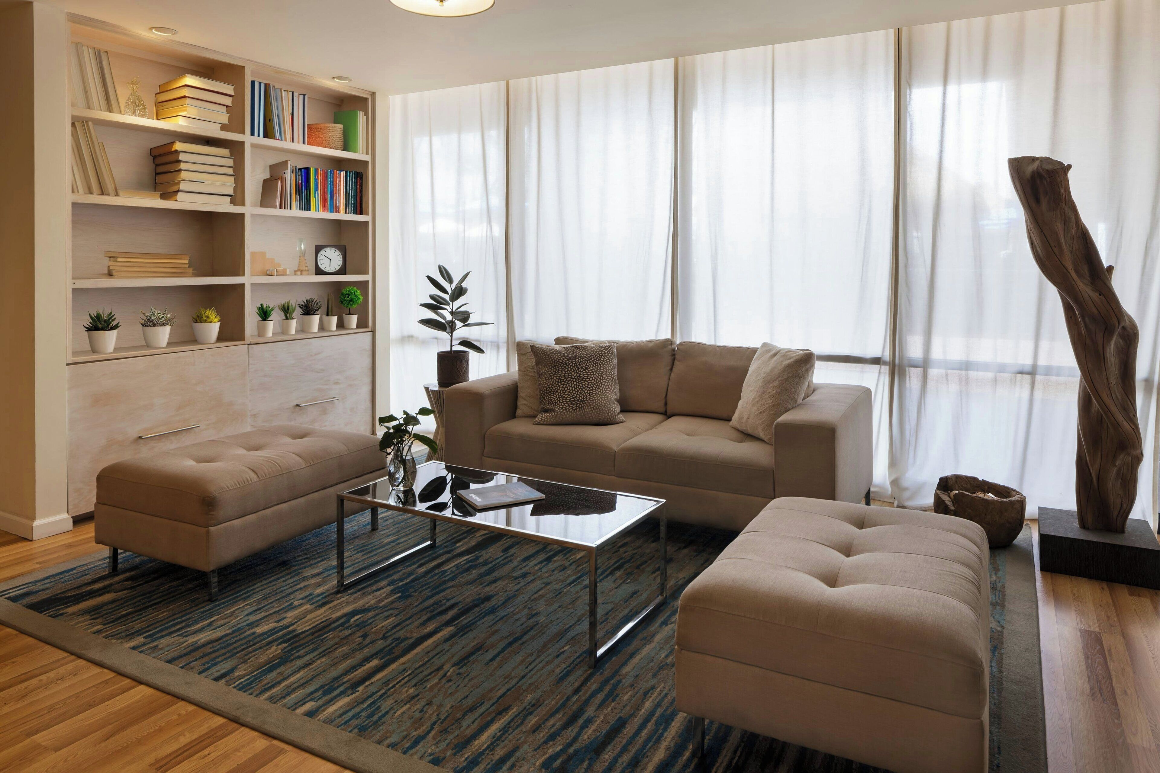 A modern living room with a sofa, ottoman, and a coffee table. There is a bookshelf with books and decorative items.