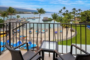 A balcony with wicker chairs overlooking a beach area with umbrellas and a dock with boats. - Courtyard by Marriott King Kamehameha's Kona Beach Hotel (Kailua-Kona)