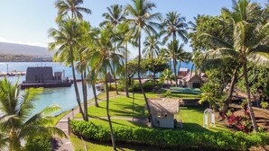 A tropical resort with a pool, palm trees, and a thatched-roof hut. - Courtyard by Marriott King Kamehameha's Kona Beach Hotel (Kailua-Kona)