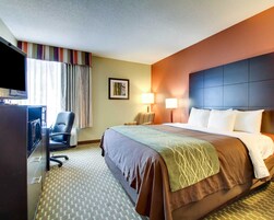 Una habitación de hotel con una cama grande, un escritorio con computadora, una silla, un televisor y una ventana con cortinas.